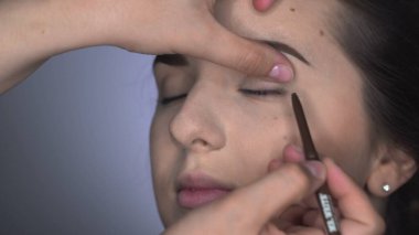 Stüdyoda oturan güzel ve muhteşem kadın için profesyonel makyaj süreci. Makyaj sanatçısı kahverengi gözlü bir kızın göz kapağına göz kalemi sürüyor.