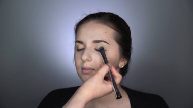 Stüdyoda oturan güzel ve muhteşem kadın için profesyonel makyaj süreci. Makyaj sanatçısı göz kapağına büyük bir fırça sürterek pudra sürüyor