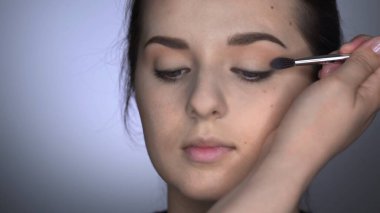 Stüdyoda oturan güzel ve muhteşem kadın için profesyonel makyaj süreci. Makyaj sanatçısı göz kapağındaki fırçayla allık sürüyor