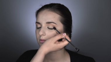 Stüdyoda oturan güzel ve muhteşem kadın için profesyonel makyaj süreci. Makyaj sanatçısı göz kapağındaki fırçayla allık sürüyor