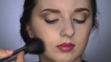 Stüdyoda oturan güzel ve muhteşem kadın için Profesyonel Makyaj. Makyaj sanatçısı tozu büyük bir fırçayla uygular
