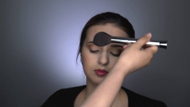 Stüdyoda oturan güzel ve güzel kadın için profesyonel makyaj. Makyaj sanatçısı tozu büyük bir fırçayla uygular