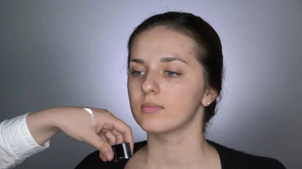 Proces af Professional Makeup for smukke og smukke kvinde sidder i studiet. Make up Kunstner anvender hudpleje creme ved hjælp af makeup børste - Stock-foto