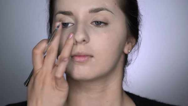 Proces af Professional Makeup for smukke og smukke kvinde sidder i studiet. Make up Kunstner anvender concealer på området nær næsen - Stock-foto