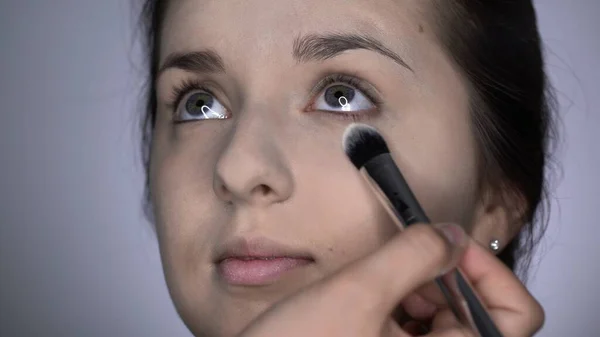 Proces af Professional Makeup for smukke og smukke kvinde sidder i studiet. Make up Kunstner anvender pulver med en stor børste på øjnene område - Stock-foto