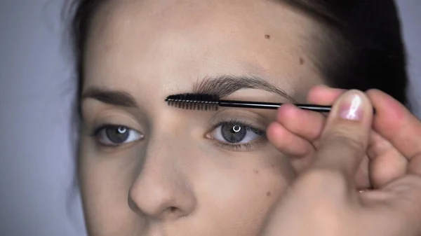 Proces af Professional Makeup for smukke og smukke kvinde sidder i studiet. Make up Kunstner makeup øjenbryn - Stock-foto
