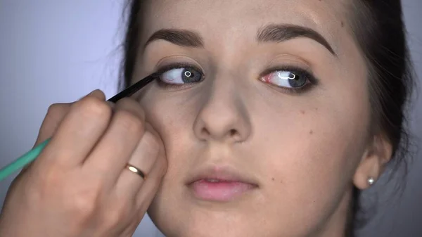 Διαδικασία Επαγγελματικού Μακιγιάζ για όμορφη και πανέμορφη γυναίκα που κάθεται στο Studio. Μακιγιάζ Καλλιτέχνης εφαρμογή eyeliner στο άνω βλέφαρο ενός κοριτσιού με καστανά μάτια — Φωτογραφία Αρχείου