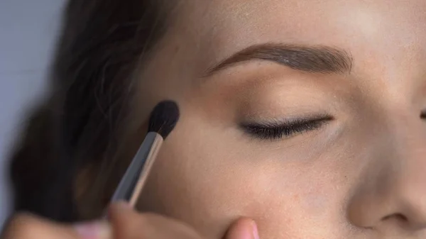 Makro skud af Professional Makeup for smukke og smukke kvinde sidder i studiet. Make up Kunstner anvender blush med pensel på øjenlåg - Stock-foto