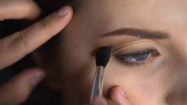 Makroaufnahme von Professional Makeup für eine schöne und hinreißende Frau, die im Studio sitzt. Make-up Artist trägt Rouge mit Pinsel auf Augenlid auf — Stockfoto