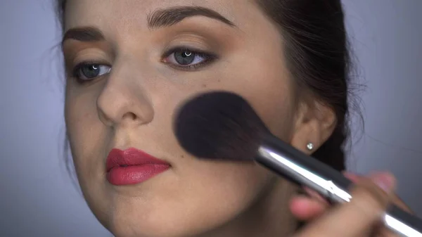 Folyamat szakmai smink gyönyörű és gyönyörű nő ül a stúdióban. Make up Artist alkalmazza por egy nagy ecset — Stock Fotó