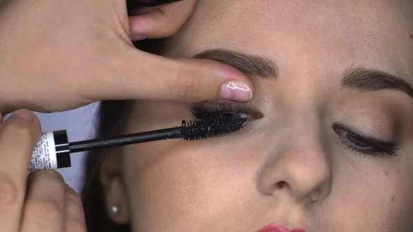 Close up de processo de maquiagem profissional para mulher bonita e linda sentada no estúdio. Maquiagem Artista aplica rímel ao modelo — Fotografia de Stock