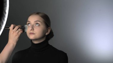 Güzellik stüdyosunda genç bir kadın için profesyonel makyaj yapıyor. Makyaj sanatçısı tozu büyük bir fırçayla uygular