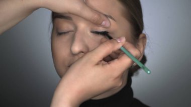 Güzellik stüdyosunda genç bir kadın için profesyonel makyaj yapıyor. Makyaj sanatçısı göz kapağına siyah göz kalemi sürüyor