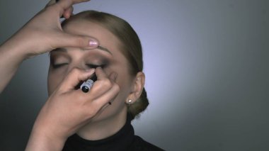 Güzellik stüdyosunda genç bir kadın için profesyonel makyaj yapıyor. Makyaj sanatçısı göz ve göz kalemi üzerine ok çizer