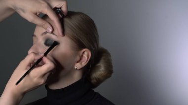 Güzellik stüdyosunda genç bir kadın için profesyonel makyaj yapıyor. Makyaj sanatçısı, siyah bir gölgenin dumanlı gözlerini güzel bir modelin özel fırçasıyla yapar