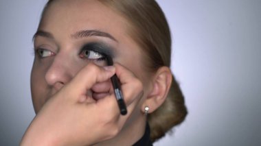 Güzellik stüdyosunda genç bir kadın için profesyonel makyaj yapıyor. Makyaj sanatçısı, siyah bir gölgenin dumanlı gözlerini güzel bir modelin özel fırçasıyla yapar
