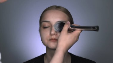 Güzellik stüdyosunda genç bir kadın için profesyonel makyaj yapıyor. Makyaj sanatçısı tozu büyük bir fırçayla uygular