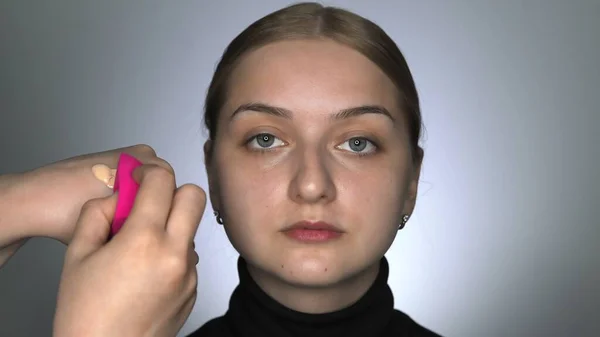 Maquillaje artista haciendo maquillaje profesional para mujer joven en el estudio de belleza. Maquillaje Artista utiliza una esponja especial para aplicar corrector en la cara — Foto de Stock