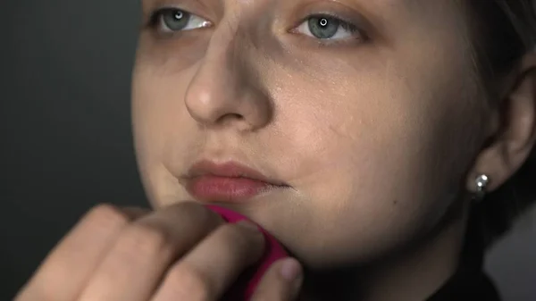 CLose up de maquilleur maquillage professionnel pour jeune femme en studio de beauté. Make up Artist utilise une éponge spéciale pour appliquer un correcteur sur le visage — Photo