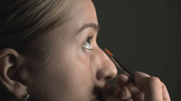 Πλευρική άποψη του make-up artist κάνοντας επαγγελματικό make-up για τη νεαρή γυναίκα στο στούντιο ομορφιάς. Make up Καλλιτέχνης εφαρμόζει concealer στην περιοχή των ματιών — Φωτογραφία Αρχείου