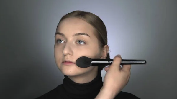 Makijażysta robi profesjonalny makijaż dla młodej kobiety w studiu kosmetycznym. Make up Artist nakłada proszek dużą szczotką — Zdjęcie stockowe
