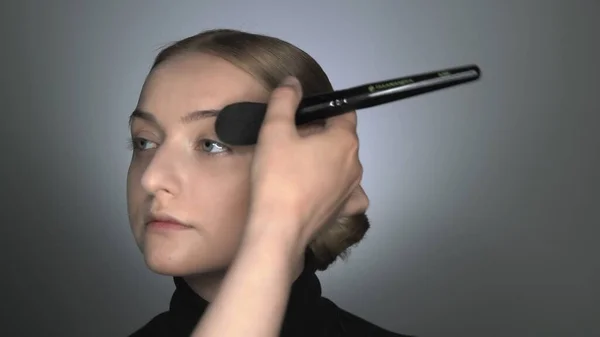 Maquillaje artista haciendo maquillaje profesional para mujer joven en el estudio de belleza. Maquillaje Artista aplica polvo con un pincel grande — Foto de Stock