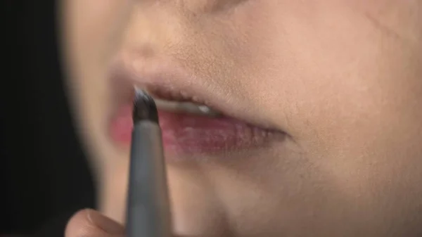 Maquillaje artista haciendo maquillaje profesional para mujer joven en el estudio de belleza. Maquillaje Artista aplica lápiz labial en los labios — Foto de Stock