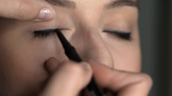 Makijażysta robi profesjonalny makijaż dla młodej kobiety w studiu kosmetycznym. Make up Artist nakłada czarny eyeliner na powiekę — Zdjęcie stockowe