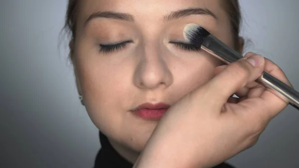 Maquillaje artista haciendo maquillaje profesional para mujer joven en el estudio de belleza. Maquillaje Artista aplica rubor con cepillo en el párpado — Foto de Stock