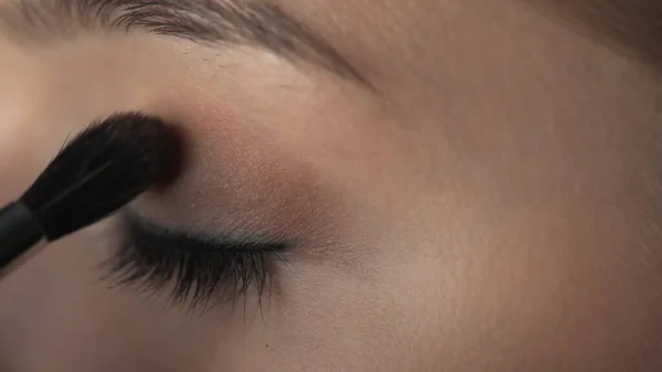 Maquillaje artista haciendo maquillaje profesional para mujer joven en el estudio de belleza. Maquillaje Artista aplica rubor con cepillo en el párpado — Foto de Stock