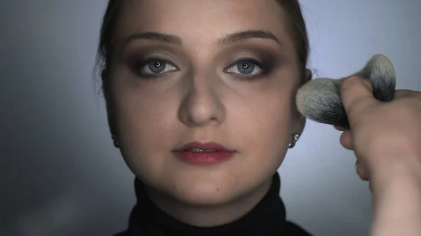 Maquillaje artista haciendo maquillaje profesional para mujer joven en el estudio de belleza. Maquillaje Artista aplica polvo con un pincel grande — Foto de Stock