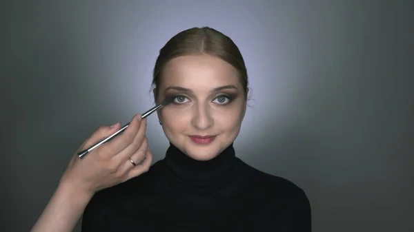 Makeup kunstner færdig med at gøre makeup til ung kvinde. Smuk kvinde med makeup ser på kameraet og poserer - Stock-foto