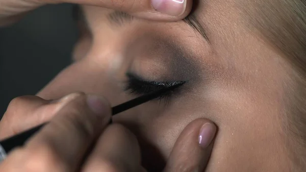 Close up de maquiador fazendo maquiagem profissional para a jovem no estúdio de beleza. Maquiagem Artista desenha flechas sobre o olho, delineador — Fotografia de Stock