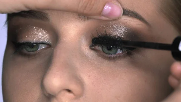 Nahaufnahme einer Visagistin, die junge Frauen im Schönheitsstudio professionell schminkt. Make-up Artist verwendet Wimperntusche — Stockfoto