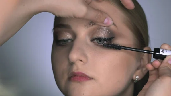 Makijażysta robi profesjonalny makijaż dla młodej kobiety w studiu kosmetycznym. Make up Artist używa tuszu do rzęs — Zdjęcie stockowe