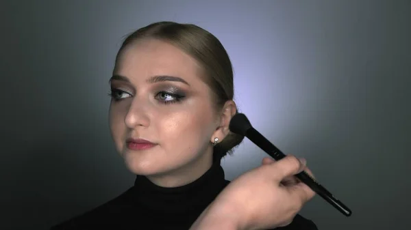 Makijażysta robi profesjonalny makijaż dla młodej kobiety w studiu kosmetycznym. Make up Artist stosuje rumieniec z dużą szczotką — Zdjęcie stockowe