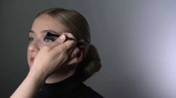 Makeup artist gør professionel make-up til ung kvinde i skønhedsstudiet. Make up Artist gør makeup smokey øjne af en sort skygge med speciel børste af en smuk model - Stock-foto