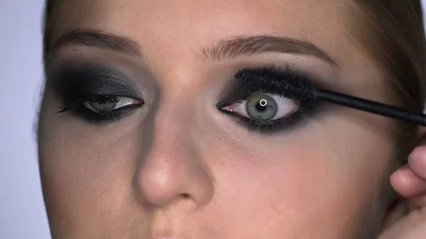 Πλευρική άποψη του καλλιτέχνη μακιγιάζ κάνει επαγγελματική make-up για νεαρή γυναίκα στο στούντιο ομορφιάς. Make up Καλλιτέχνης ζωγραφίζει μάσκαρα βλεφαρίδες — Φωτογραφία Αρχείου