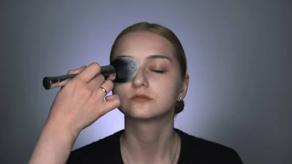 Maquillaje artista haciendo maquillaje profesional para mujer joven en el estudio de belleza. Maquillaje Artista aplica polvo con un pincel grande — Foto de Stock