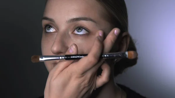 Visagistin, die junge Frauen im Schönheitsstudio professionell schminkt. Make-up Artist trägt Concealer auf Augenpartie auf — Stockfoto