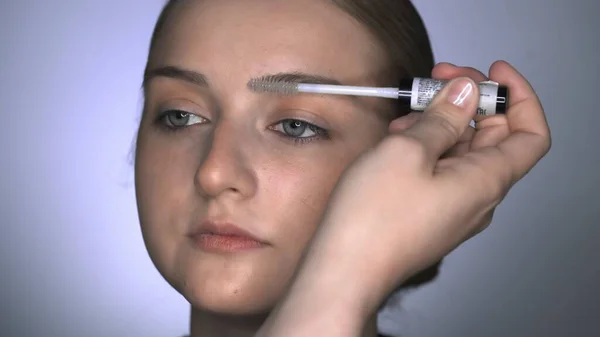 Macro de maquillaje artista haciendo maquillaje profesional para mujer joven en el estudio de belleza. Maquillaje Artista utiliza cepillo para las cejas — Foto de Stock