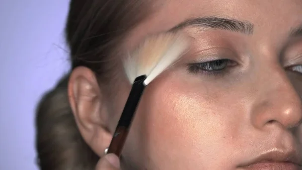Güzellik stüdyosunda genç bir kadın için profesyonel makyaj yapıyor. Makyaj sanatçısı parlatıcı ya da vurgu yapmak için fırça kullanır