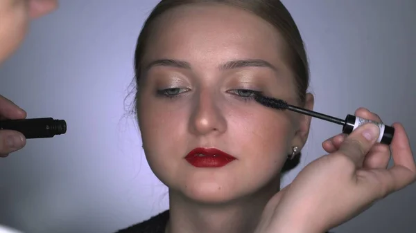 Makeup artist making professional make-up για νεαρή γυναίκα στο στούντιο ομορφιάς. Make up Καλλιτέχνης ζωγραφίζει μάσκαρα βλεφαρίδες — Φωτογραφία Αρχείου