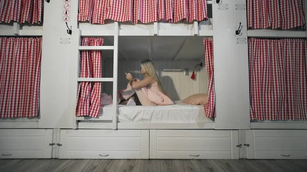 Junge attraktive Frau sitzt auf dem Bett im Hostel-Zimmer und nutzt Smartphone — Stockfoto