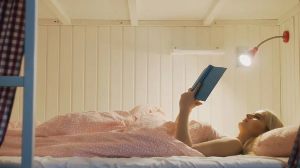 Woman in night underwear finished read book, turns light off and goes to sleep in cozy hostel room