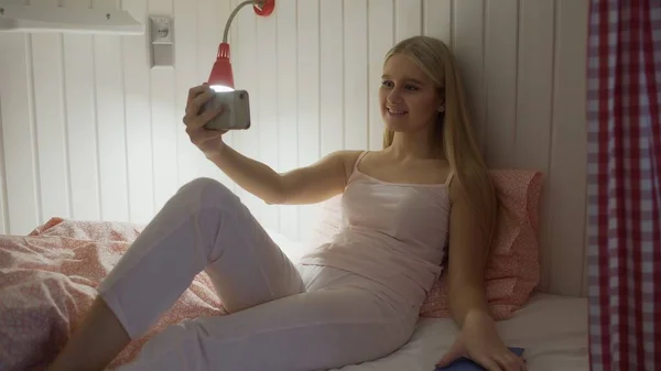Närbild av ung attraktiv kvinna som sitter på sängen i vandrarhemsrummet och använder smartphone med videochatt — Stockfoto