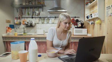 Dizüstü bilgisayarda çalışan ve mısır gevreği yiyen genç bir kadın..