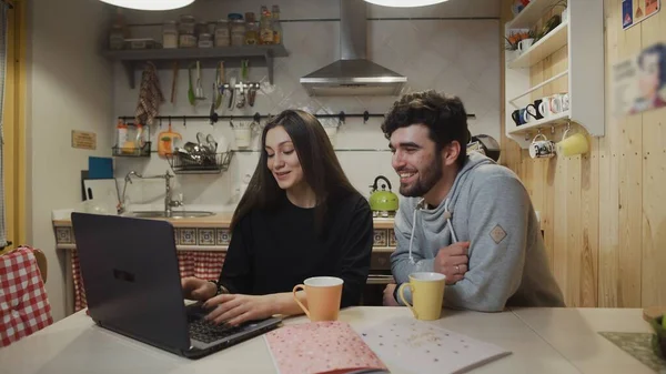 Smiling couple drinking coffee at kitchen. Joyful couple watching laptop computer. Happy man talking with woman at kitchen. — Stock Photo, Image