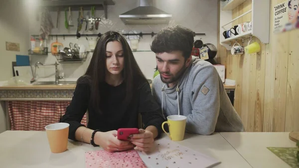 Mladý pár snídá v kuchyni. Radostný pár sledující obrazovku chytrého telefonu. Šťastný muž mluví se ženou v kuchyni. — Stock fotografie