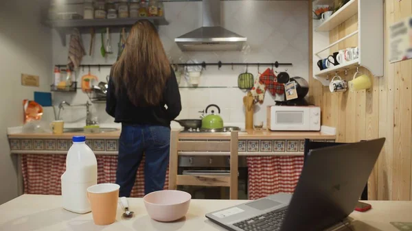 Junge Frau arbeitet am Laptop und isst Cornflakes-Müsli in der heimischen Küche. — Stockfoto
